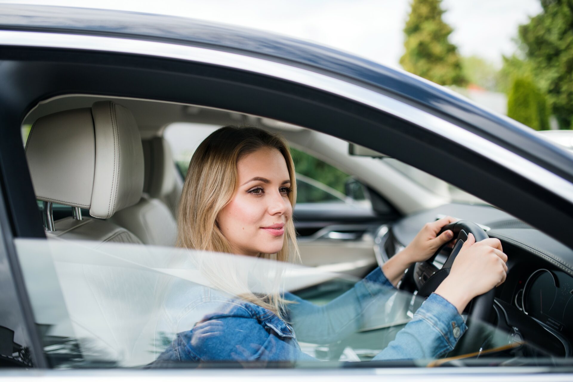 A happy young woman driver sitting in car, waiting.